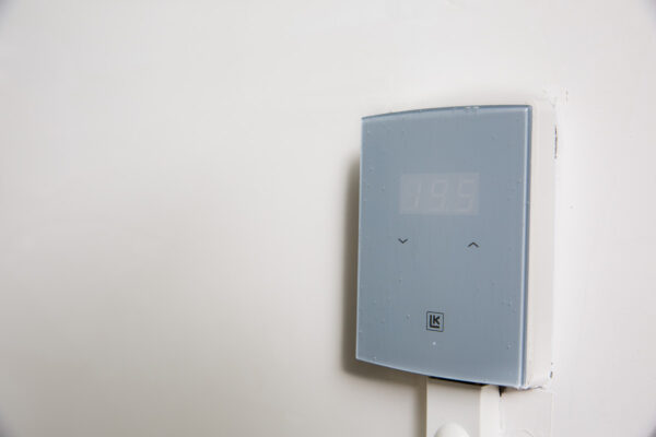 Grijze LK thermostaat gemonteerd aan een witte muur op Laan van S-Gravenmade, met een afleesbare temperatuur van 19,5 graden.